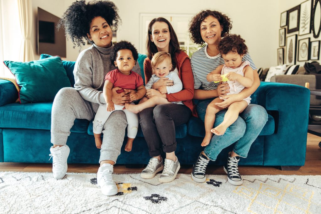 Multi-ethnic parents sitting with children. Young parents with babies sitting on sofa and looking at camera.